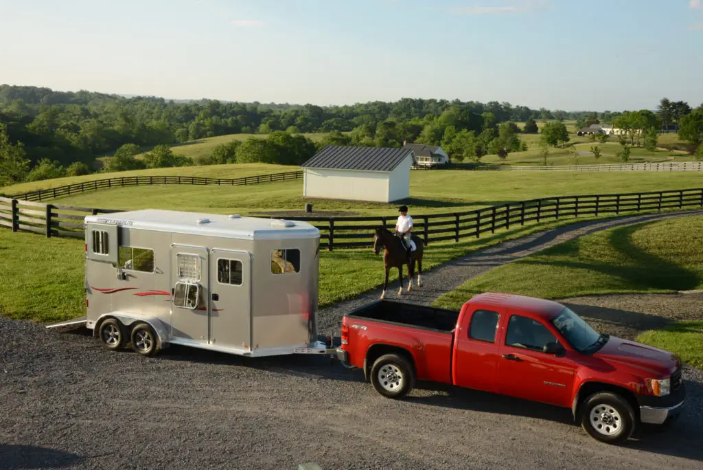 Imagen de un camión y un remolque de caballos en una granja de caballos cerca de un caballo y un jinete,